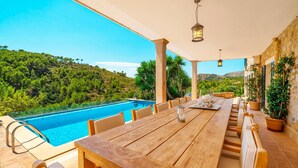 A wooden table and chairs set up outdoors with a view of a swimming pool and a mountainous landscape. - Cozy home in Andratx with private swimming pool, can be inside or outside (Andratx)