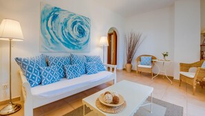 Ein modernes Wohnzimmer mit einem weißen Sofa, gemusterten Kissen, einem Couchtisch und einem blauen, abstrakten Gemälde an der Wand.