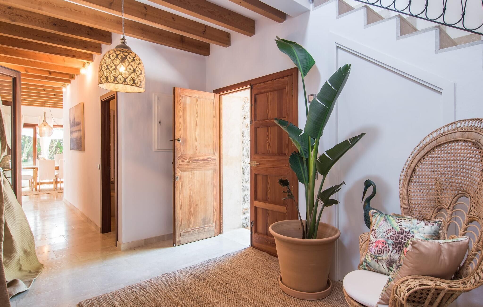 A cozy interior with a wooden door, a potted plant, and a wicker chair with cushions.