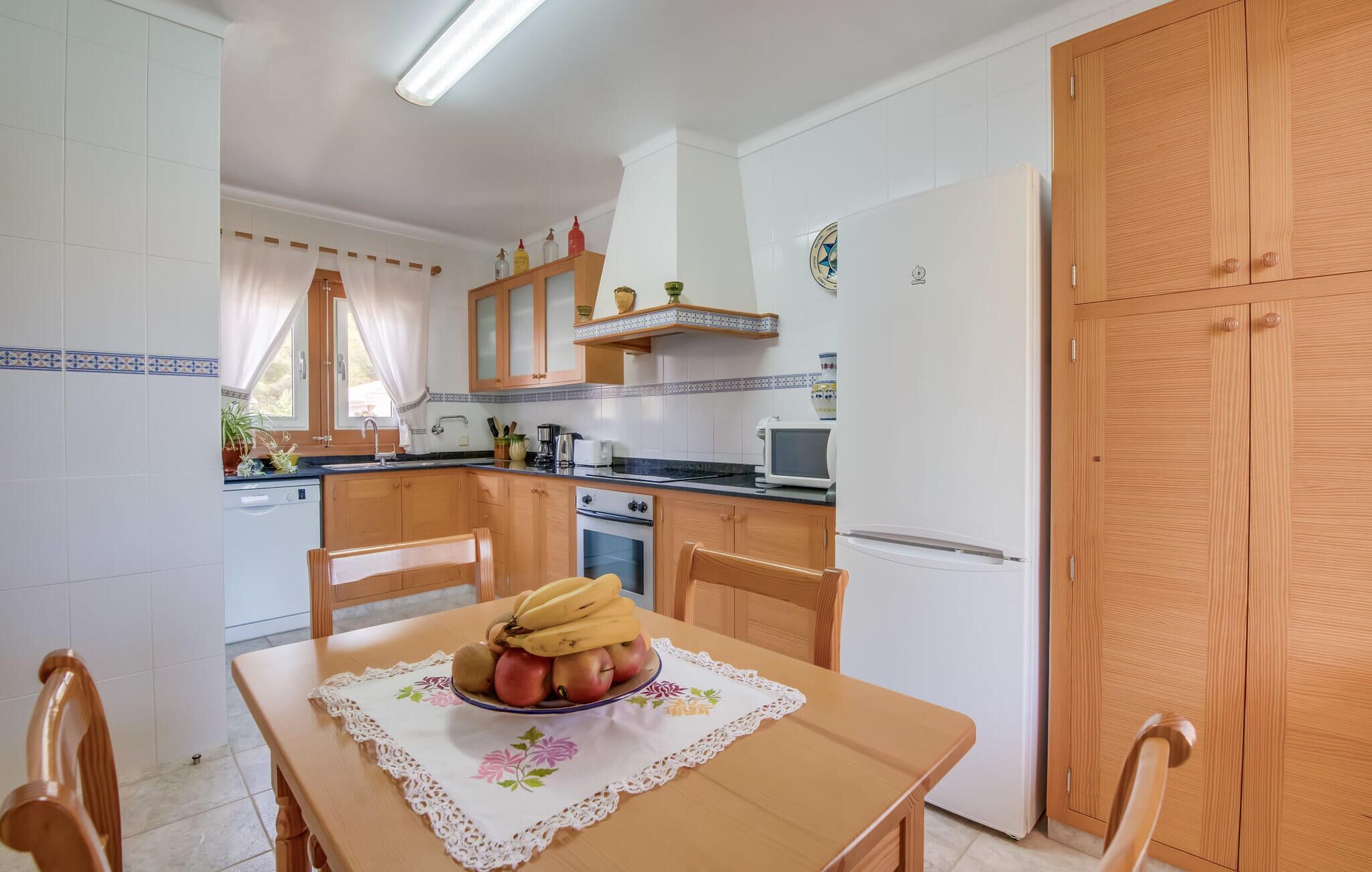 Cocina compacta con muebles de madera, microondas y refrigerador. En primer plano, una mesa de comedor con un frutero.