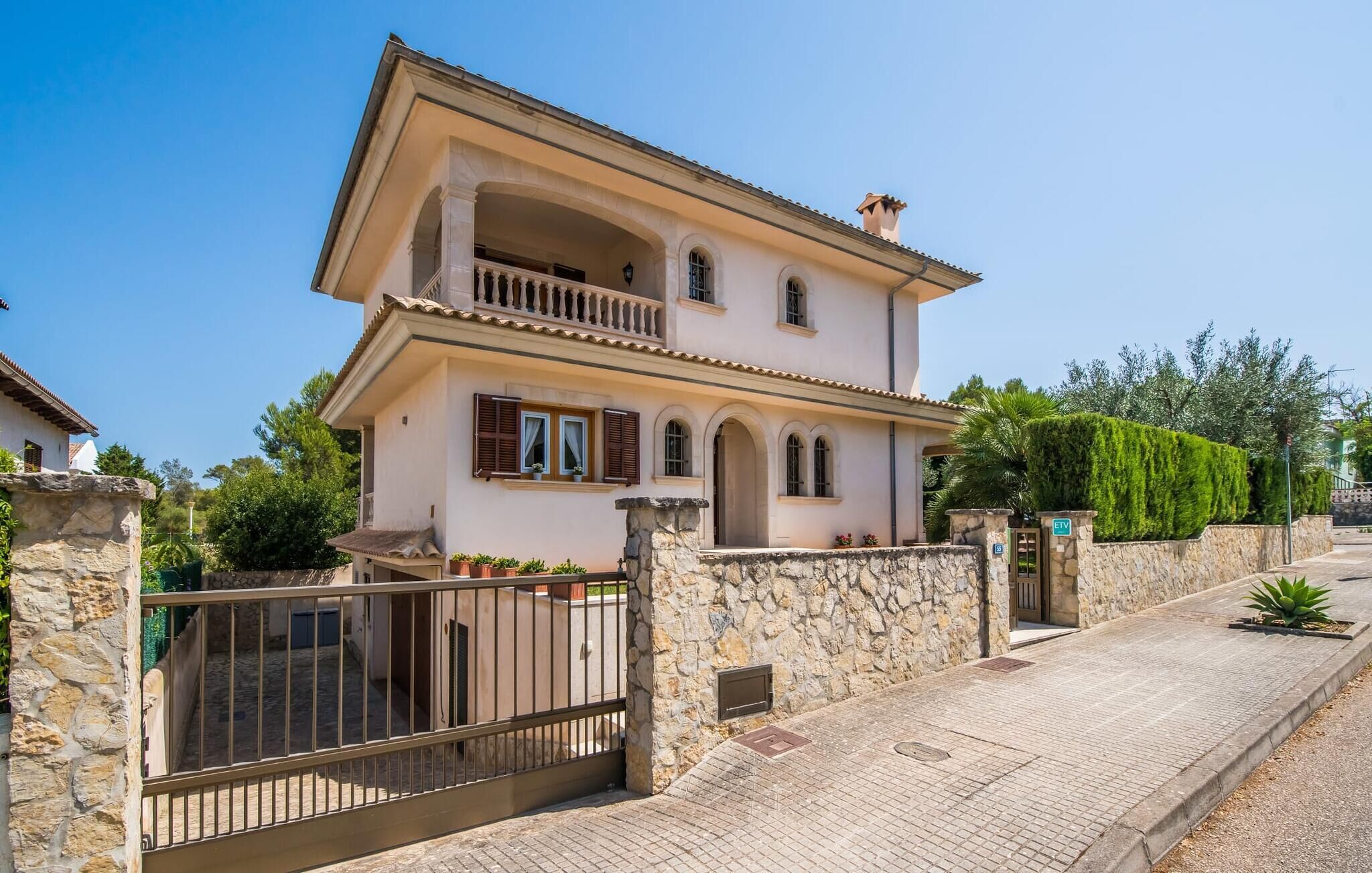 A two-story house with a balcony, stone walls, and a gated entrance.