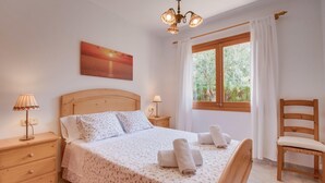 A bedroom with a wooden bed, two bedside tables, a nightstand, a chair, a window with curtains, and a painting on the wall. - Calma de Son Serra de Marina (Son Serra de Marina)