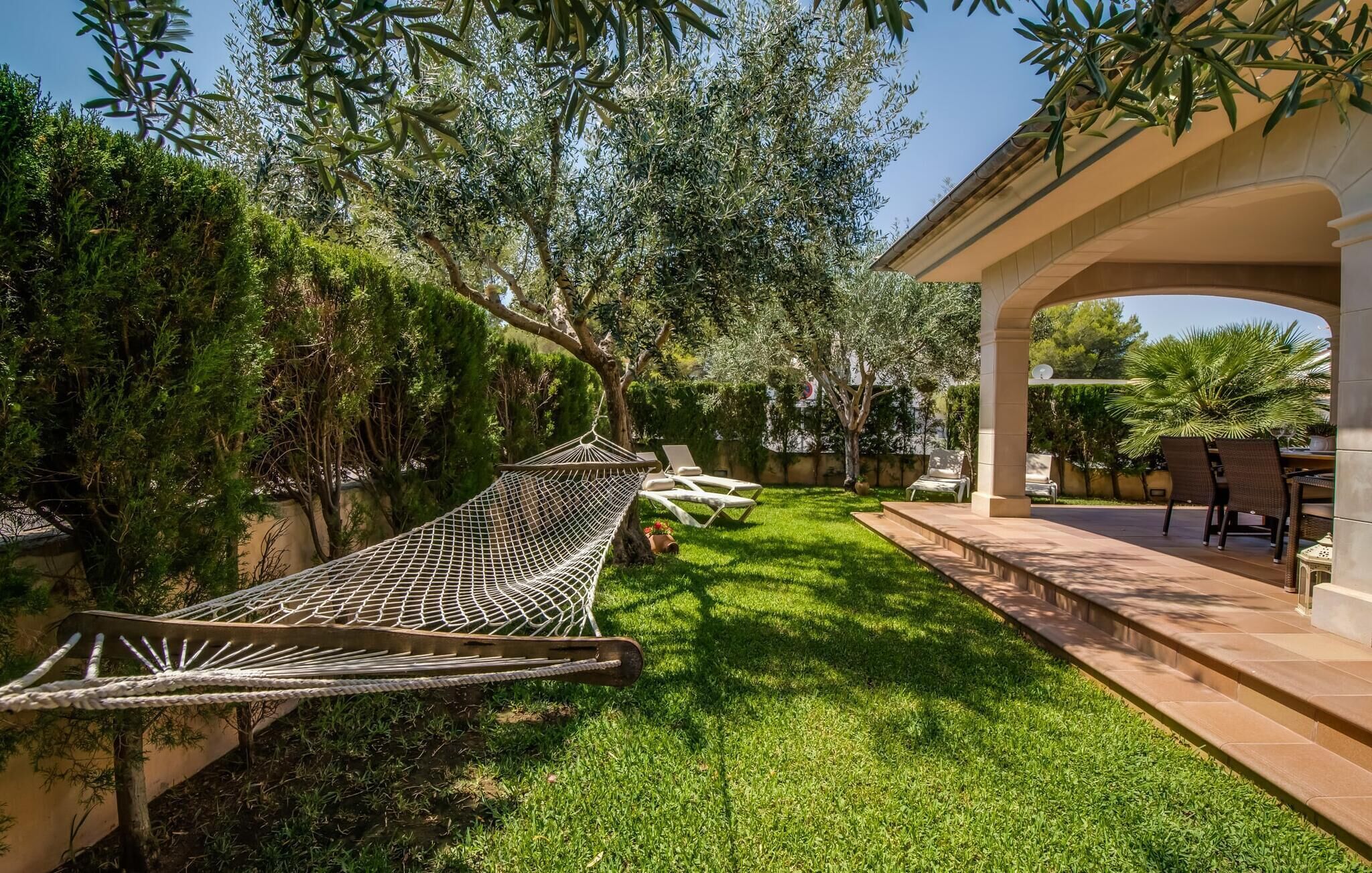 A hammock in a lush garden with a pergola and outdoor seating area.