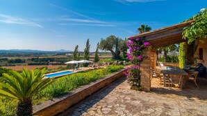 Un área de piscina con vistas al campo, una pérgola con asientos y un muro de piedra.