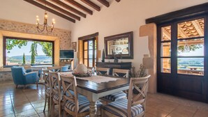 Un comedor con una mesa grande, sillas y televisor. Se ven vistas del campo a través de las ventanas.