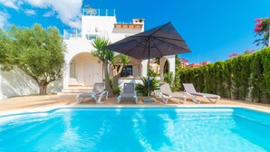 A swimming pool with lounge chairs and an umbrella, surrounded by greenery and a white building with arches. - Gorgeous home in Badia Blava (Badia Blava)