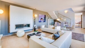 Ein modernes Wohnzimmer mit Kamin, weißen Sofas, einem Couchtisch und einer Treppe, die in eine andere Ebene führt.