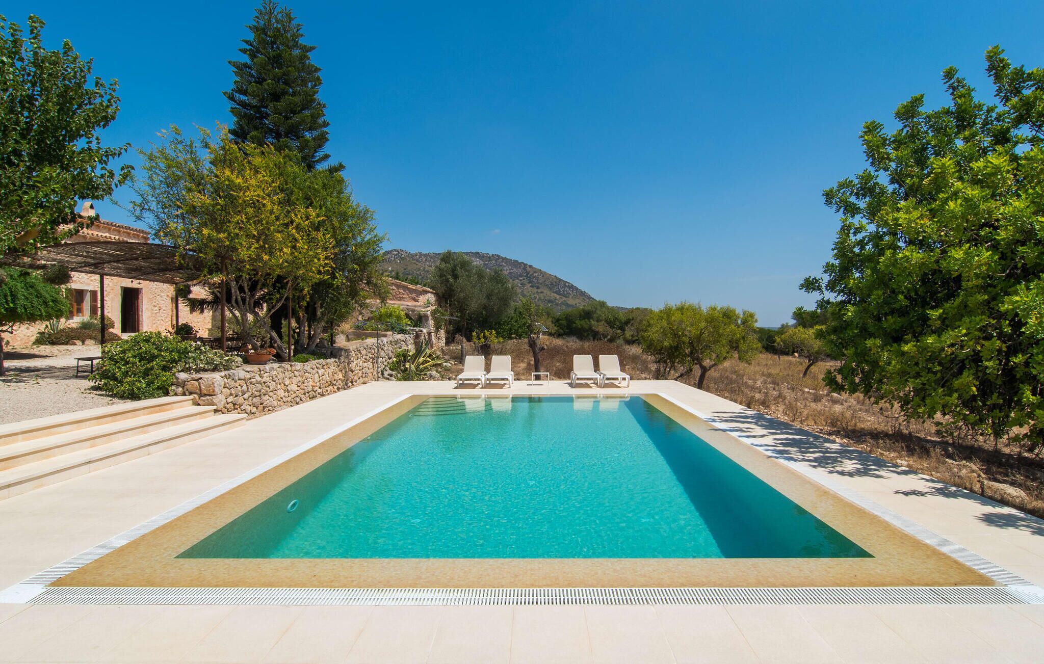 A rectangular swimming pool with clear blue water, surrounded by a stone deck and white lounge chairs.