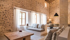 A rustic stone-walled room with a wooden table, a sofa, and a dining area with chairs. - Gorgeous home in Sant Llorenc (Sant Llorenc)