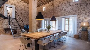 A spacious dining area with a wooden table and modern chairs, set against a stone wall backdrop. - Gorgeous home in Sant Llorenc (Sant Llorenc)