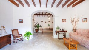 Una sala de estar acogedora con techo de madera, una escalera que sube a otra habitación, un sillón mecedor, un sofá y una máquina de coser.