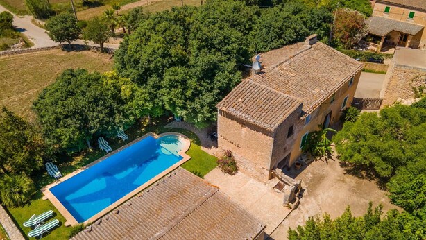Vista aérea de una propiedad con piscina, edificio de piedra y follaje circundante.