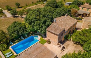 Vista aérea de una propiedad con piscina, edificio de piedra y follaje circundante.