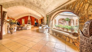 A spacious living area with a high arched ceiling, stone walls, and a view of a courtyard with plants and a hammock. - Cozy home in Santanyi with private swimming pool, can be inside or outside (Santanyi)