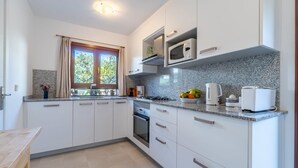 Una cucina moderna con mobili bianchi, un piano di lavoro in granito, un forno a microonde, un bollitore e una ciotola di frutta.