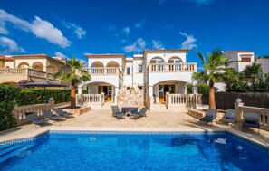 A poolside area with lounge chairs, a stone wall, and a clear blue sky. - 3 bedroom stunning home in Cala Pi (Cala Pi)