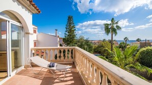 Ein Balkon mit weißem Stuhl, einer Glastür und Blick auf das Meer und Palmen.