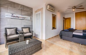 A room with a bed, two wicker chairs, a small table, a wall-mounted air conditioner, a ceiling fan, and a large window. - Stunning home in Cala Pi with house sea view (Cala Pi)