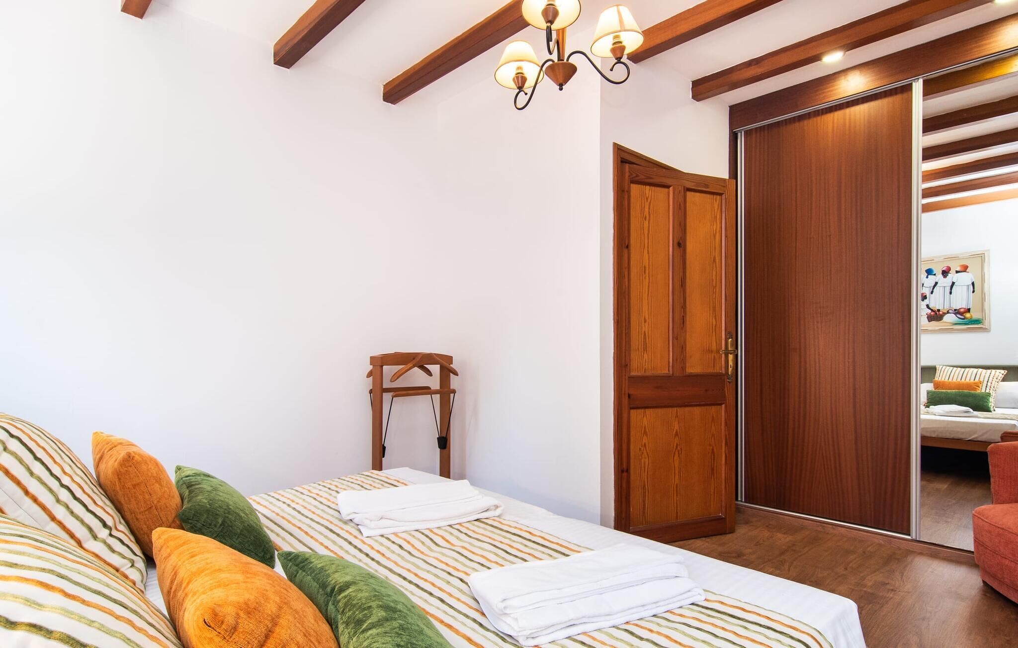 A bedroom with a bed, pillows, a wooden wardrobe, and a painting on the wall.