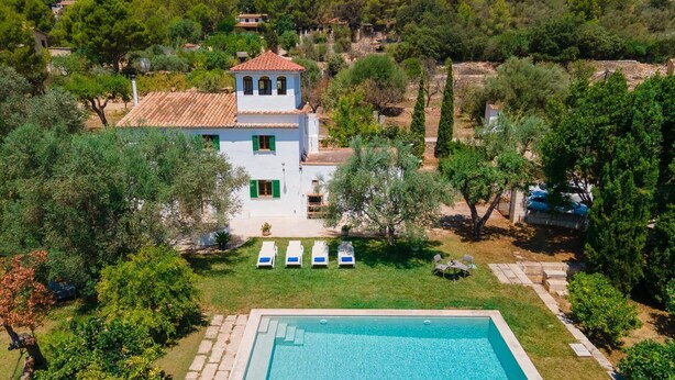 Une villa blanche avec un toit en tuiles, une piscine et un jardin agrémenté de chaises longues.