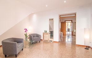 A spacious living area with a grey sofa, a glass coffee table, and a vase with flowers. A wooden cabinet with drawers is visible, and a door leads to a balcony. - Stunning apartment in Son Carrio with WiFi (Son Carrio)
