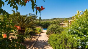 A garden pathway leading to a pool, surrounded by lush greenery and a thatched-roof structure. - Nice home in Cas Concos des Cavalle (Cas Concos des Cavalle)