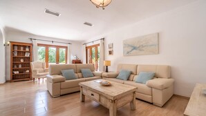A spacious living room with a beige sofa set, a wooden coffee table, and a bookshelf. - Lovely home in Cala Mendia with private swimming pool, can be inside or outside (Cala Mendia)