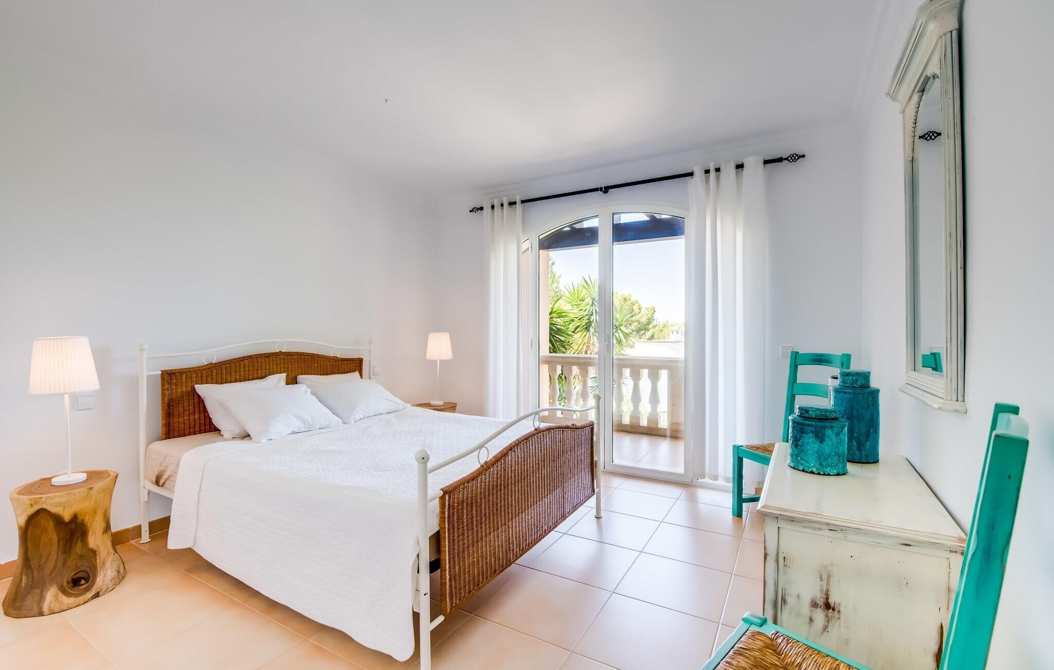 Un dormitorio con cama, mesitas de noche, cómoda, una silla y un balcón con cortinas.