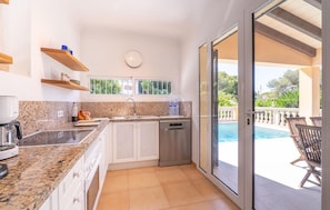 A modern kitchen with granite countertops, a built-in dishwasher, and a window overlooking a pool area. - Beach front home in Capdepera (Capdepera)