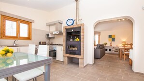 Une cuisine moderne dotée d’une cuisinière intégrée, un coin repas avec une table en verre et un salon agrémenté d’une cheminée.