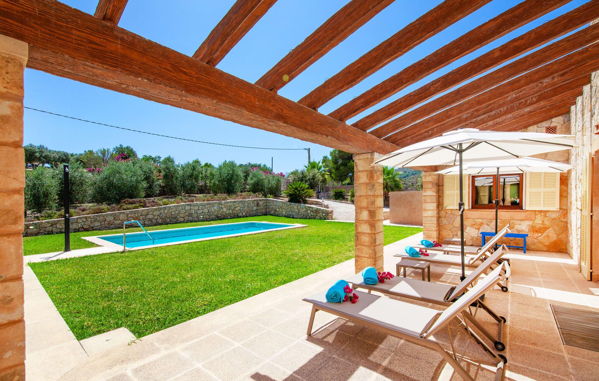 Un espacio al aire libre cubierto con piscina, sillas de descanso y un muro de piedra.