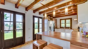 Een moderne keuken met houten balken, grote ramen en een centraal kookeiland met barkrukken.