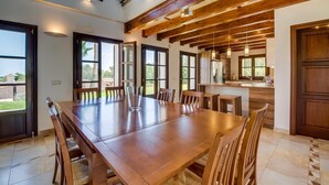 Een ruime eethoek met een grote houten tafel en stoelen, een keuken met houten balken en grote ramen met uitzicht op de omgeving.