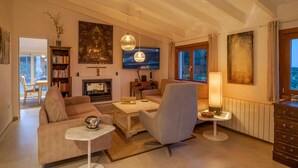 Un salon chaleureux avec une cheminée, des fauteuils confortables, un téléviseur et des œuvres d’art accrochées aux murs.