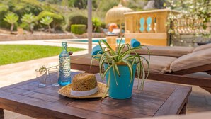 Une table en bois, sur laquelle se trouvent un chapeau de paille, une bouteille bleue et une plante en pot.