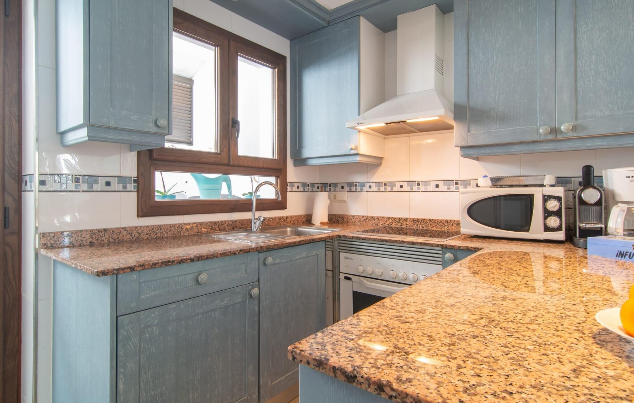 A kitchen with granite countertops, a microwave, a stove, and blue cabinets.