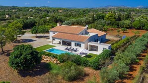 Una villa moderna con piscina, rodeada de exuberante vegetación y una vista panorámica de colinas.