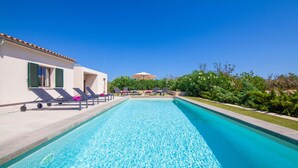 Una piscina con sillones de descanso y un edificio con contraventanas verdes.