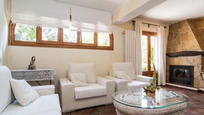 A living room with a stone fireplace, white sofas, and a glass coffee table. - Awesome home in Cala Ratjada (Cala Ratjada)