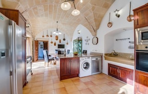 A spacious kitchen with a stone ceiling, a washing machine, a sink, and a dining area with a table and chairs. - Amazing home in Santanyi with private swimming pool, can be inside or outside (Santanyi)