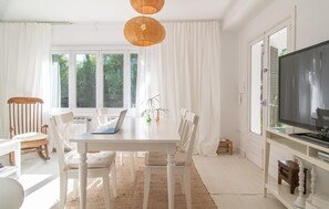 A bright, white room with a dining table, chairs, a laptop, and a TV. - Beautiful home in Cala Millor (Cala Millor)