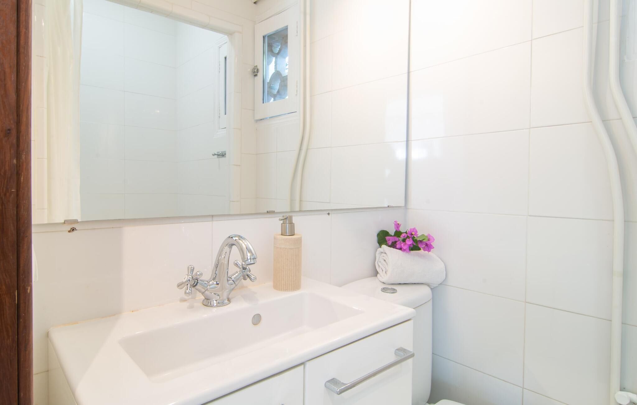 A bathroom with a white sink, a mirror, and a towel rack with a pink flower.