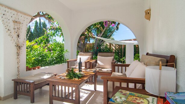 A sunlit patio with wooden furniture, a table, and books. - Beautiful home in Cala Millor (Cala Millor)