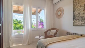 A bedroom with a bed, a chair, a small table, and a window with curtains. - Beautiful home in Cala Millor (Cala Millor)