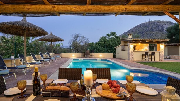 Un espace extérieur avec une piscine, des chaises longues, un coin repas avec de la vaisselle et un bar dont l’intérieur est illuminé.