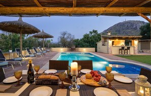 An outdoor pool area with lounge chairs, a dining setup with tableware, and a bar area with a lit-up interior. - Cozy home in Alcudia with private swimming pool, can be inside or outside (Alcudia)