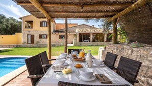Un espace de restauration en plein air avec une table dressée pour le petit-déjeuner, donnant sur une piscine et un bâtiment en pierre.