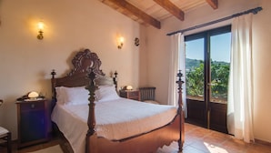 A bedroom with a wooden four-poster bed, a nightstand, a lamp, and a view of the outdoors through a sliding glass door. - Cozy home in Son Macia with private swimming pool, can be inside or outside (Son Macia)