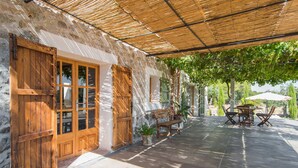 A covered outdoor patio with stone walls, wooden furniture, and a pergola providing shade. - Gorgeous home in Canyamel with private swimming pool, can be inside or outside (Canyamel)