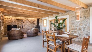 A rustic interior with exposed wooden beams, stone walls, a stone fireplace, wicker furniture, and a dining table with chairs. - Gorgeous home in Canyamel with private swimming pool, can be inside or outside (Canyamel)